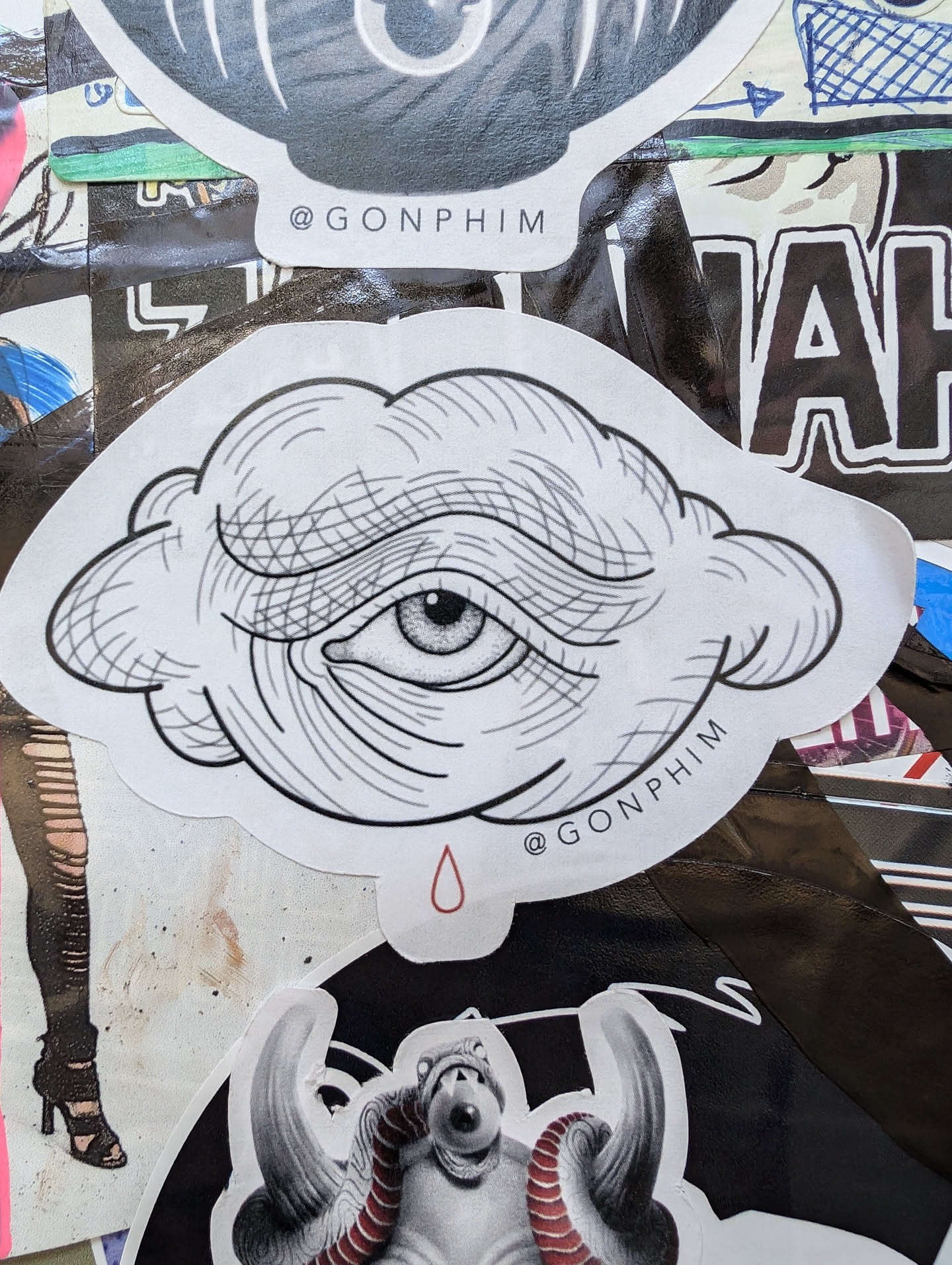 A monochrome illustration of an eye inside a cloud with a single red teardrop below. The style is reminiscent of traditional tattoo flash. The artist's Instagram handle is visible on the sticker.