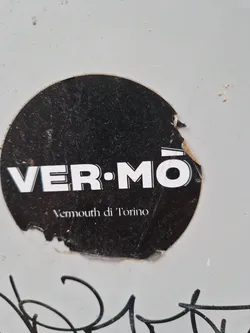 A round black and white sticker with the text VERMŌ and Vermouth di Torino. The sticker is slightly damaged.