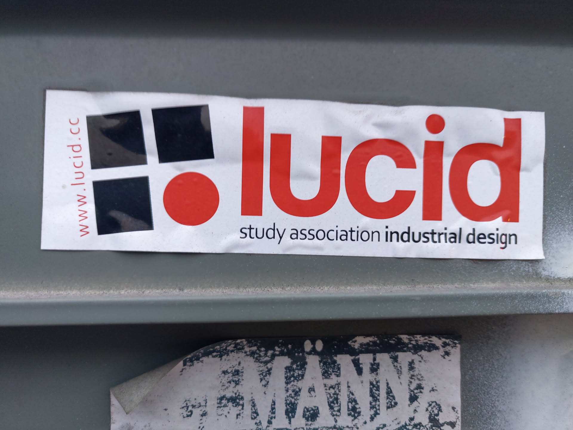 A sticker for Lucid, a study association for industrial design.  The sticker features a logo with black squares and a red circle, along with the association's name and website.