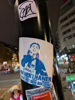 A rectangular blue and white sticker featuring a graphic stencil of a person with long hair making a 'shushing' gesture with their index finger over their lips. The figure wears a Hertha BSC jersey adorned with the club's flag crest and an 'ACAB' print. Bold German text across the bottom reads 'KEIN HERTHANER QUATSCHT MIT DEN BULLEN!'.