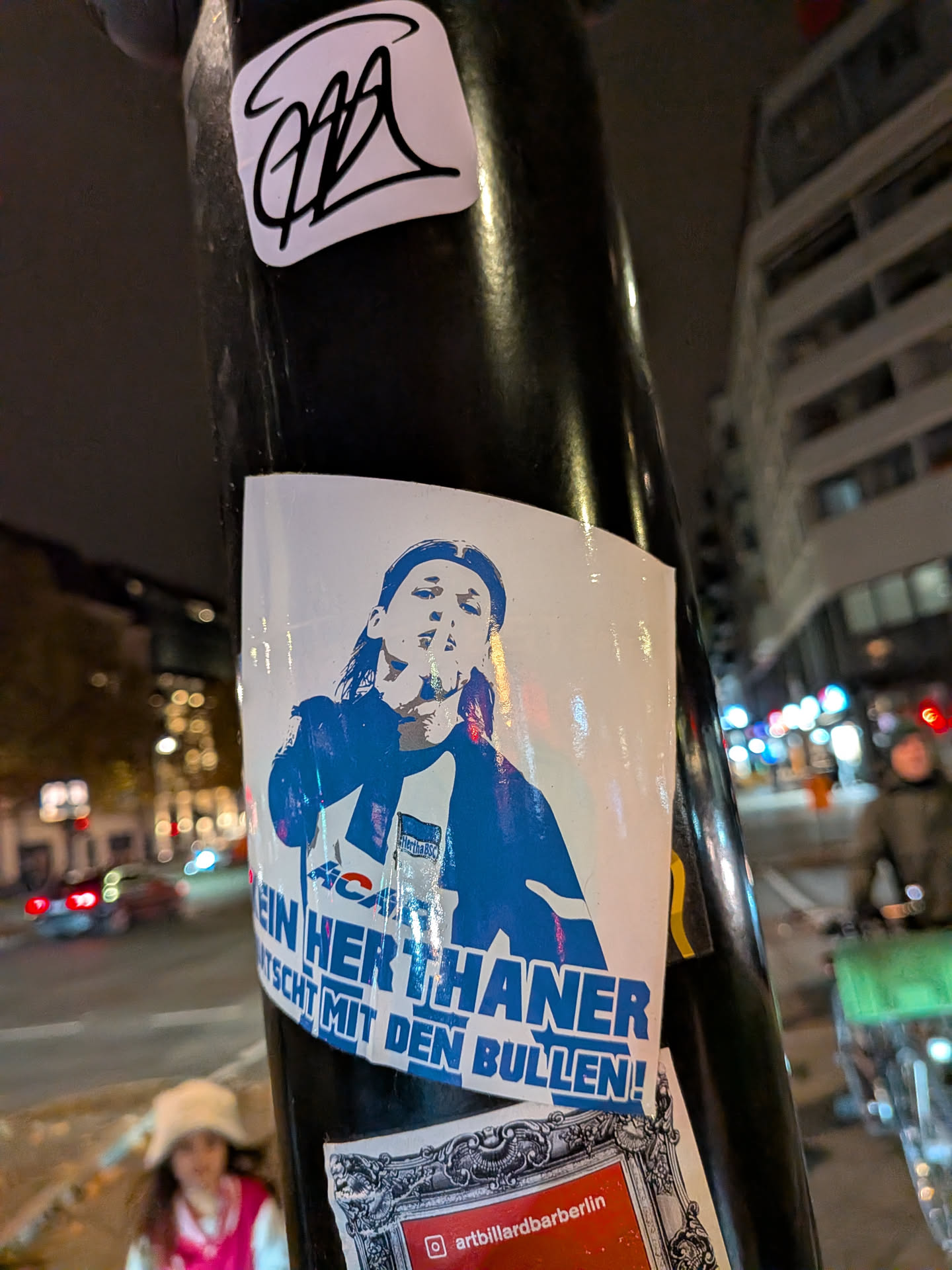A rectangular blue and white sticker featuring a graphic stencil of a person with long hair making a 'shushing' gesture with their index finger over their lips. The figure wears a Hertha BSC jersey adorned with the club's flag crest and an 'ACAB' print. Bold German text across the bottom reads 'KEIN HERTHANER QUATSCHT MIT DEN BULLEN!'.