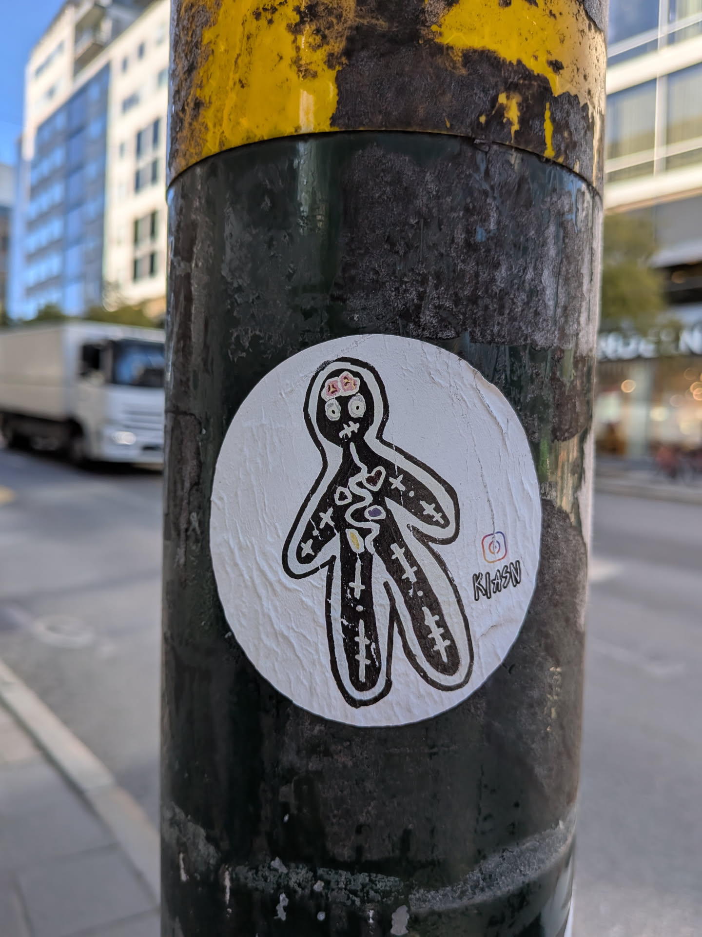 The sticker is circular and white, with a black outline. It depicts a simplified, stick-figure-like human form with visible internal organs. The head contains a pink and red representation of a brain with some details. The torso shows a heart and other organ-like shapes, drawn with black lines and some color infill. The limbs are also outlined in black. To the right of the figure, there is a small Instagram logo followed by the text 'KIXSN' in a stylized font. The sticker appears slightly crinkled and adhered to a dark, textured surface.