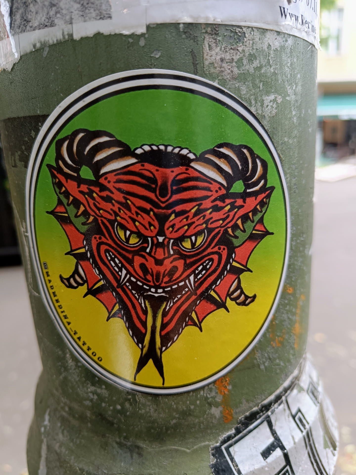 Round sticker featuring a traditional Japanese oni mask with yellow, red and green colors. The text "MADMEDINA_TATTOO" is visible at the bottom. 
