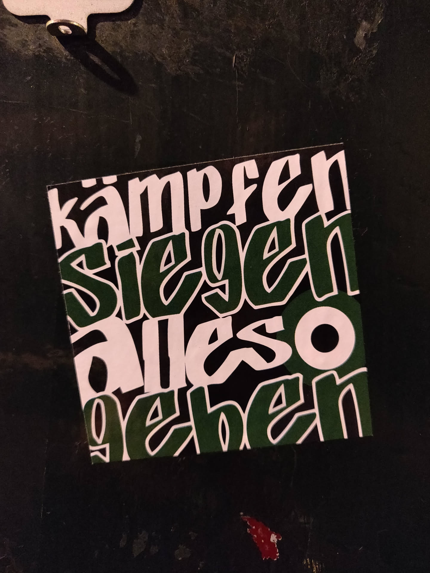 A dark green and white sticker with German text. The text is stylized in a graffiti-like font.  The words translate to "fight win give everything".