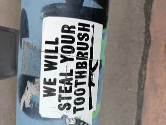 A sticker on a pole with a threatening message and an image of a gun. The sticker is torn and weathered.