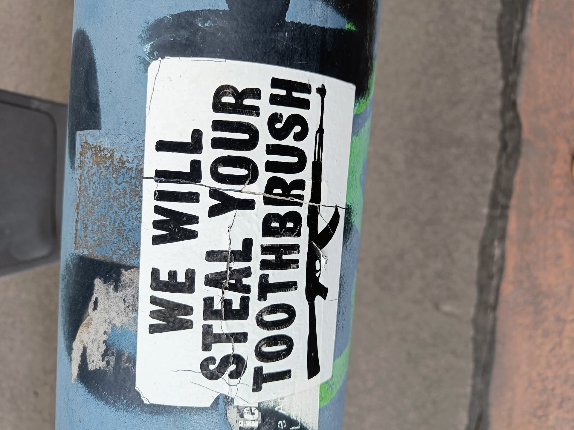 A sticker on a pole with a threatening message and an image of a gun. The sticker is torn and weathered.