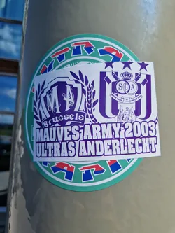 A sticker featuring the logo of Mauves Army 2003, the ultras group of Anderlecht. The sticker also includes the logos of two other groups. The main colors are purple and white.