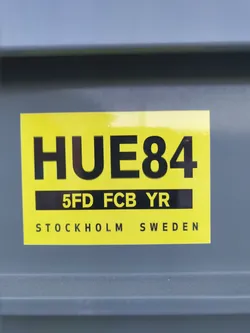 A yellow and black sticker with the text HUE84, 5FD FCB YR, and Stockholm Sweden. 