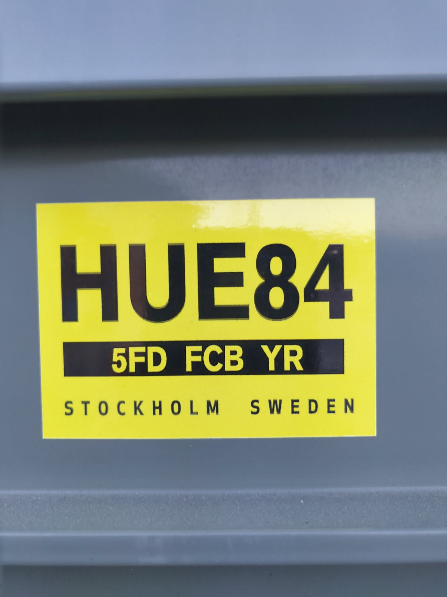 A yellow and black sticker with the text HUE84, 5FD FCB YR, and Stockholm Sweden. 
