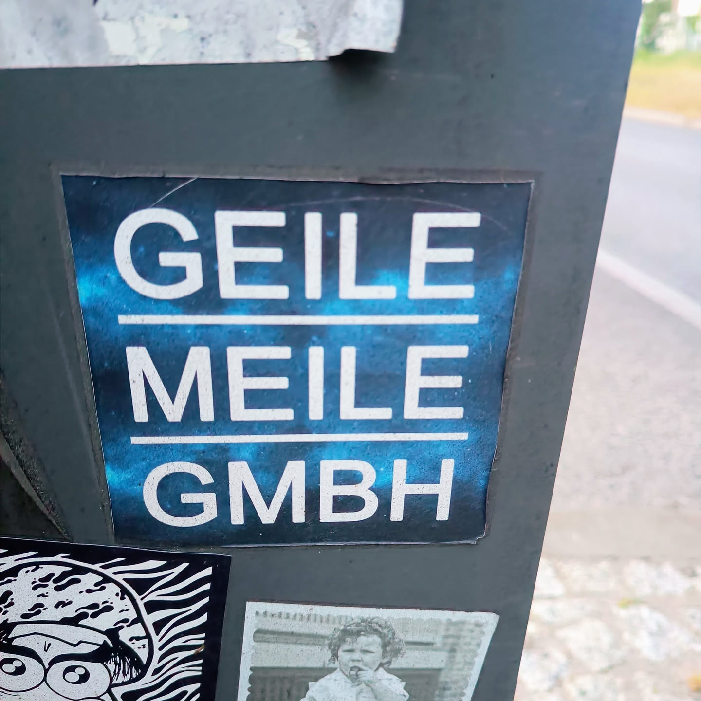 A sticker with the text "GEILE MEILE GMBH" on a blue nebula background.  The text is in white, with each word on a separate line. GMBH is a common abbreviation for a limited liability company in German.