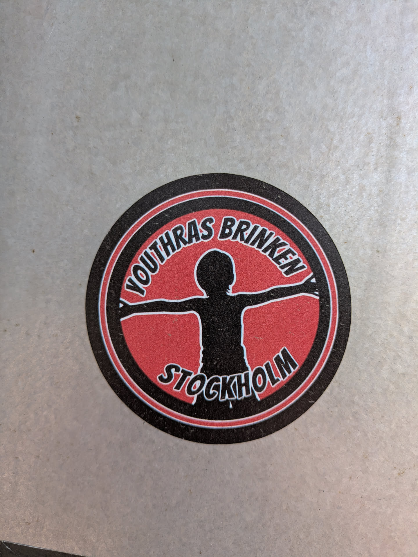 This is a round sticker with a black and red design. The text 'YOUTHRAS BRINKEN' is written on the top part of the circle and 'STOCKHOLM' on the bottom part. In the center is a silhouette of a person with arms outstretched.