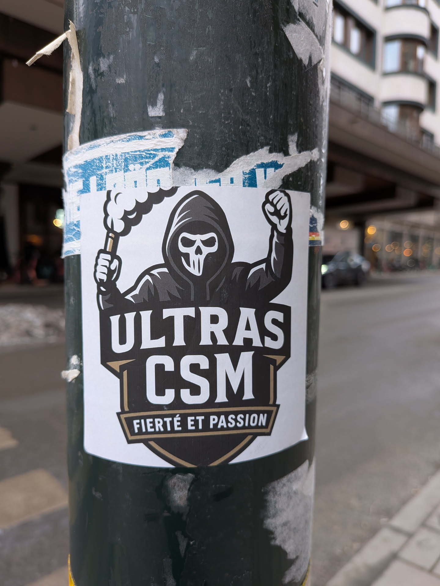 A bold sticker featuring a central figure in a dark hooded sweatshirt and a white skull mask. The figure holds a smoking flare in its left hand and a clenched fist raised in its right. The text 'ULTRAS' is prominently displayed above 'CSM' in large white letters, both set against a black banner with gold/bronze accents. Below 'CSM', a smaller banner reads 'FIERTÉ ET PASSION' in white text. The overall design is graphic and striking, using a limited palette of black, white, and gold/bronze, set against a white background.