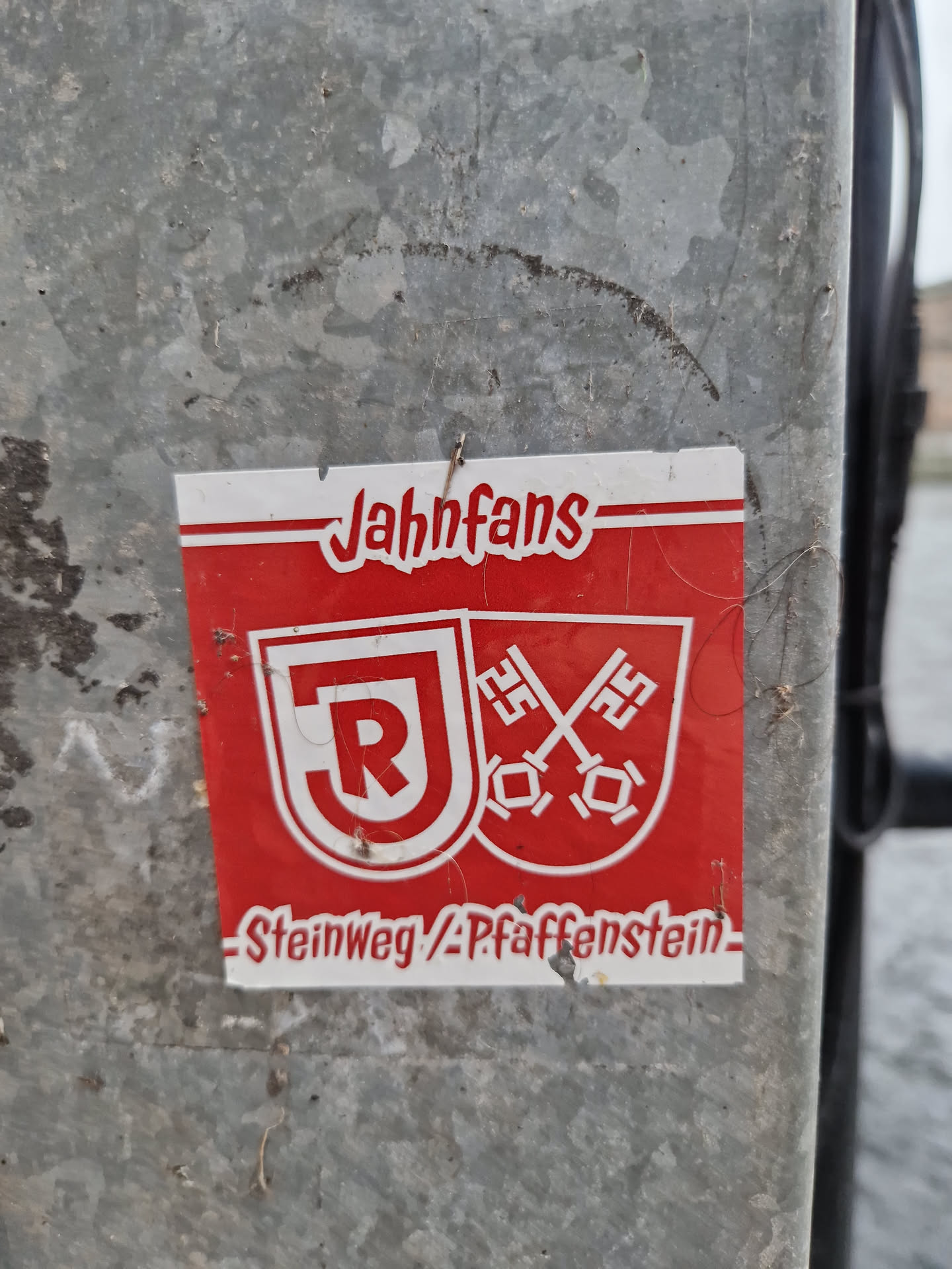 Red and white sticker with the text "Jahnfans" at the top and  "Steinweg/Pfaffenstein" at the bottom.  A logo with the letters "JR" and crossed keys is in the center.