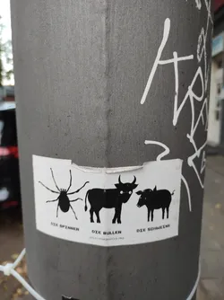 A black and white sticker affixed to a grey pole, depicting a spider, a bull, and a pig in a simple, almost minimalist style.  Each animal has German text below it: "Die Spinnen", "Die Bullen", and "Die Schweine".