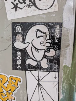 Street sticker A square monochrome sticker featuring a stylized cartoon fish character outlined in thick black with a white body, depicted standing on two small feet with fins outstretched and an expressive, determined face. The background is solid black, filled with Japanese text in white: '魚' (fish) inside a circle in the upper left, '魚の侵入' (fish invasion) running vertically down the left side, '世界的に' (worldwide/globally) running vertically on the upper right, and a boxed exclamation mark '!' on the bottom right. At the bottom edge, small text reads 'MERIOONE * FISHES INVASION'. The sticker shows slight surface tears and weathering.