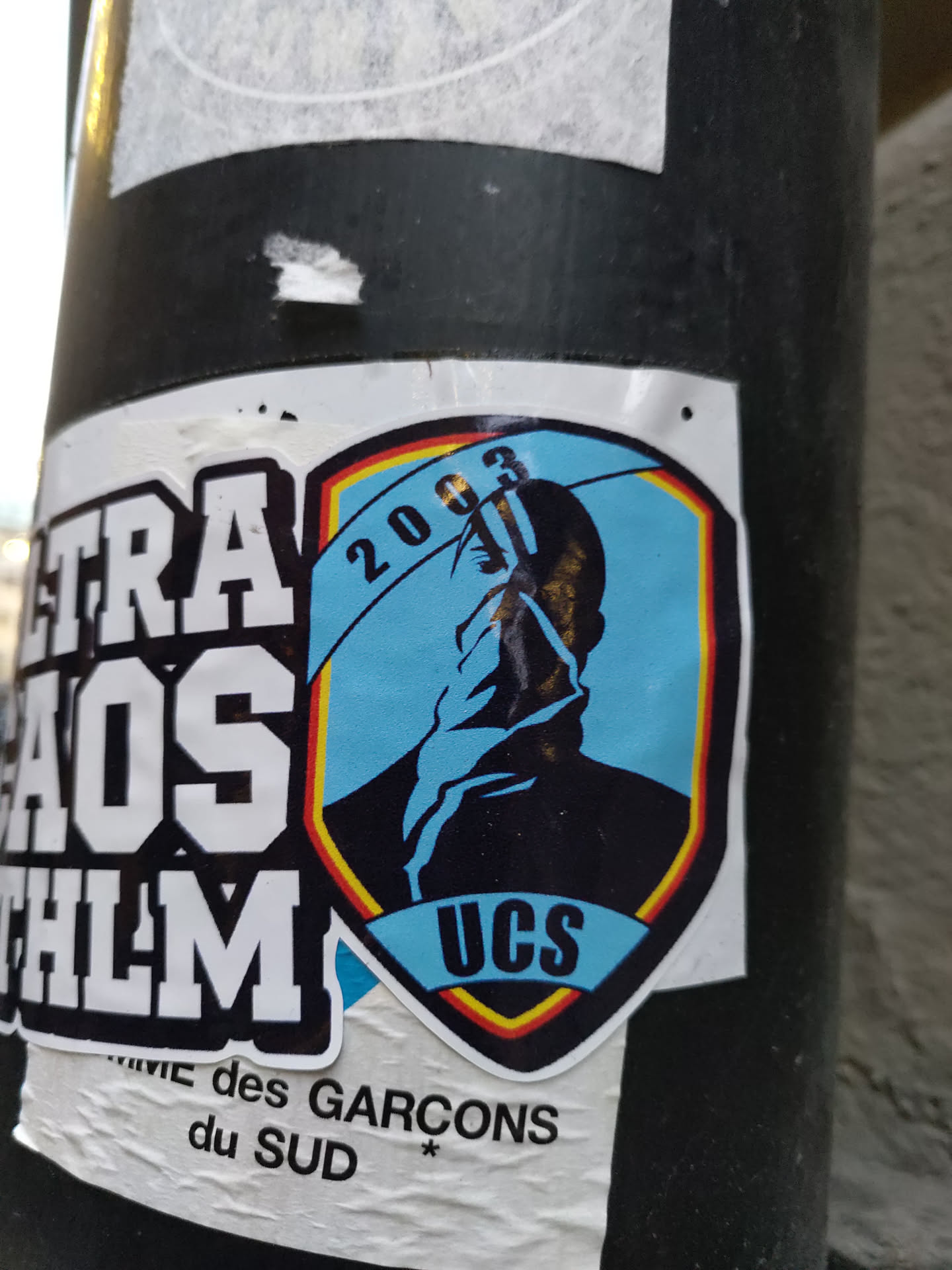 A sticker featuring a shield-shaped logo with a silhouette of a person, the year 2003, and the abbreviation UCS.  There is additional text visible that says "Ultras Chaos Film" and part of what appears to be French text below. 