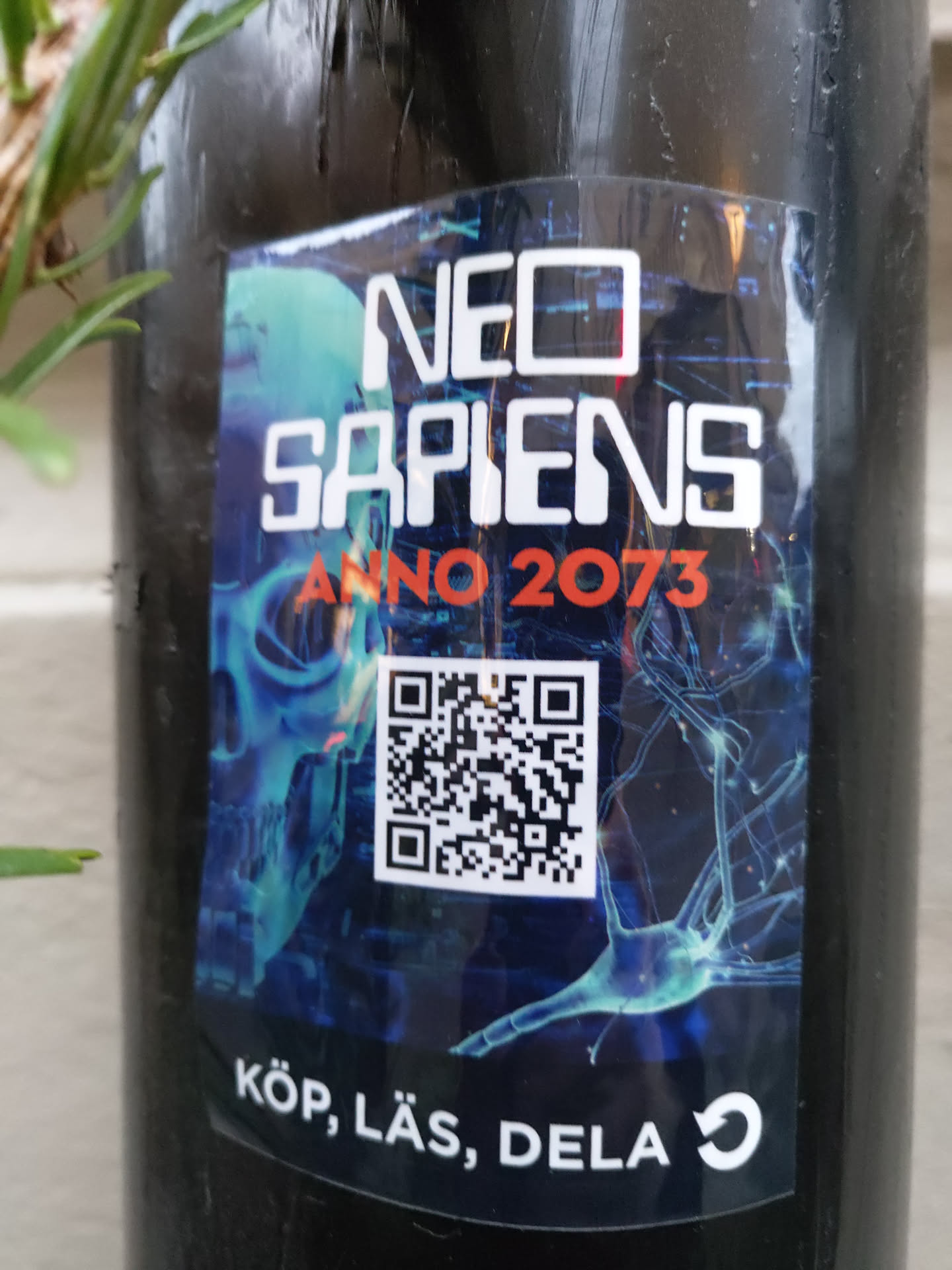 A futuristic sticker with a dark blue and black color scheme. It features a stylized skull, neural network imagery, and a QR code. The text on the sticker says "Neo Sapiens Anno 2073" and "Köp, Läs, Dela" (Buy, Read, Share).