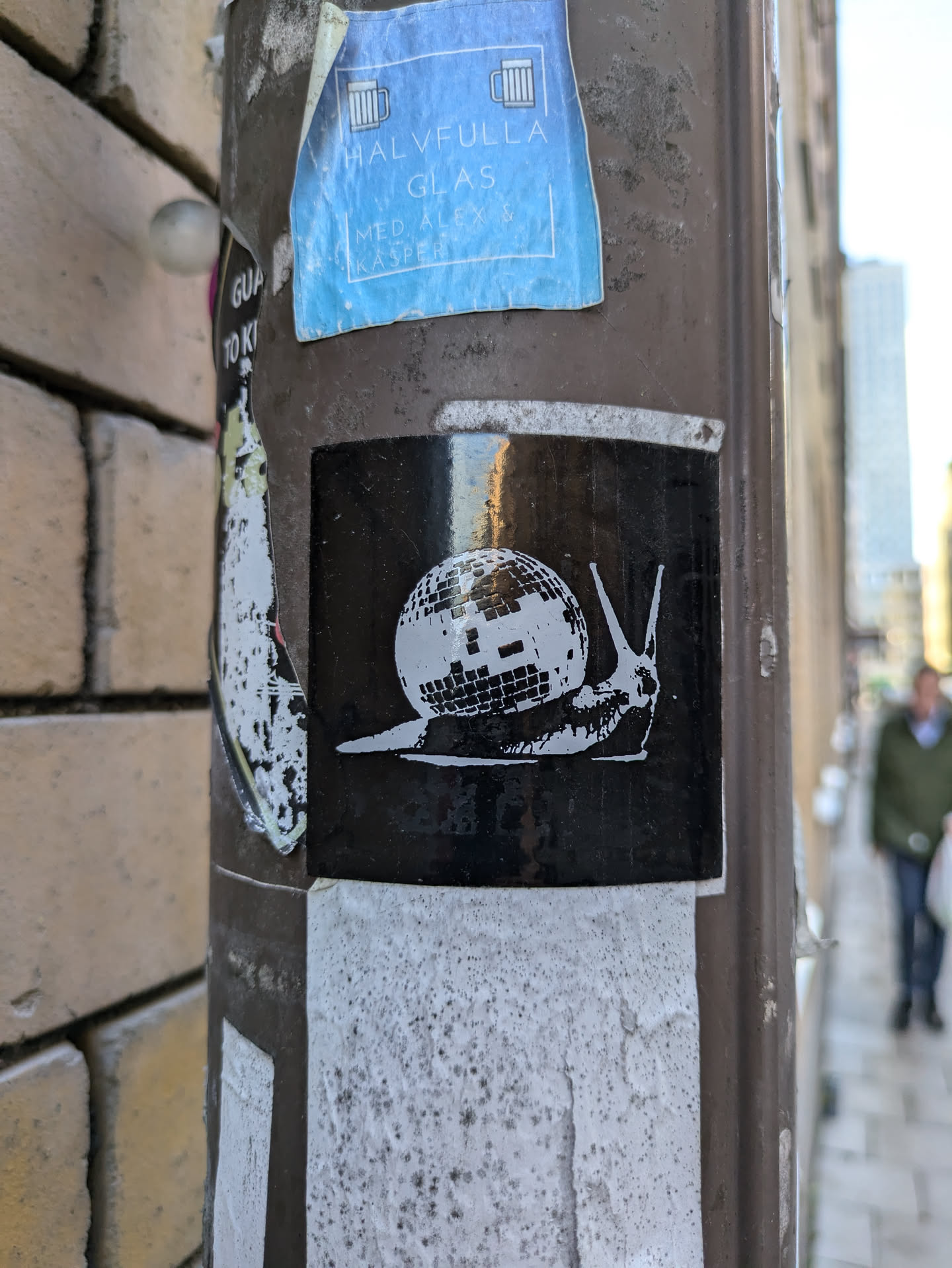 A black and white sticker of a snail carrying a disco ball on its back. The sticker is affixed to a brown pole.