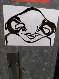 Black and white sticker featuring a stylized creature with a smooth, almost alien-like face. The creature's expression is subtle, neither happy nor sad, making it intriguing and mysterious. The artwork is minimalistic yet striking, using bold lines and negative space to create a memorable image.