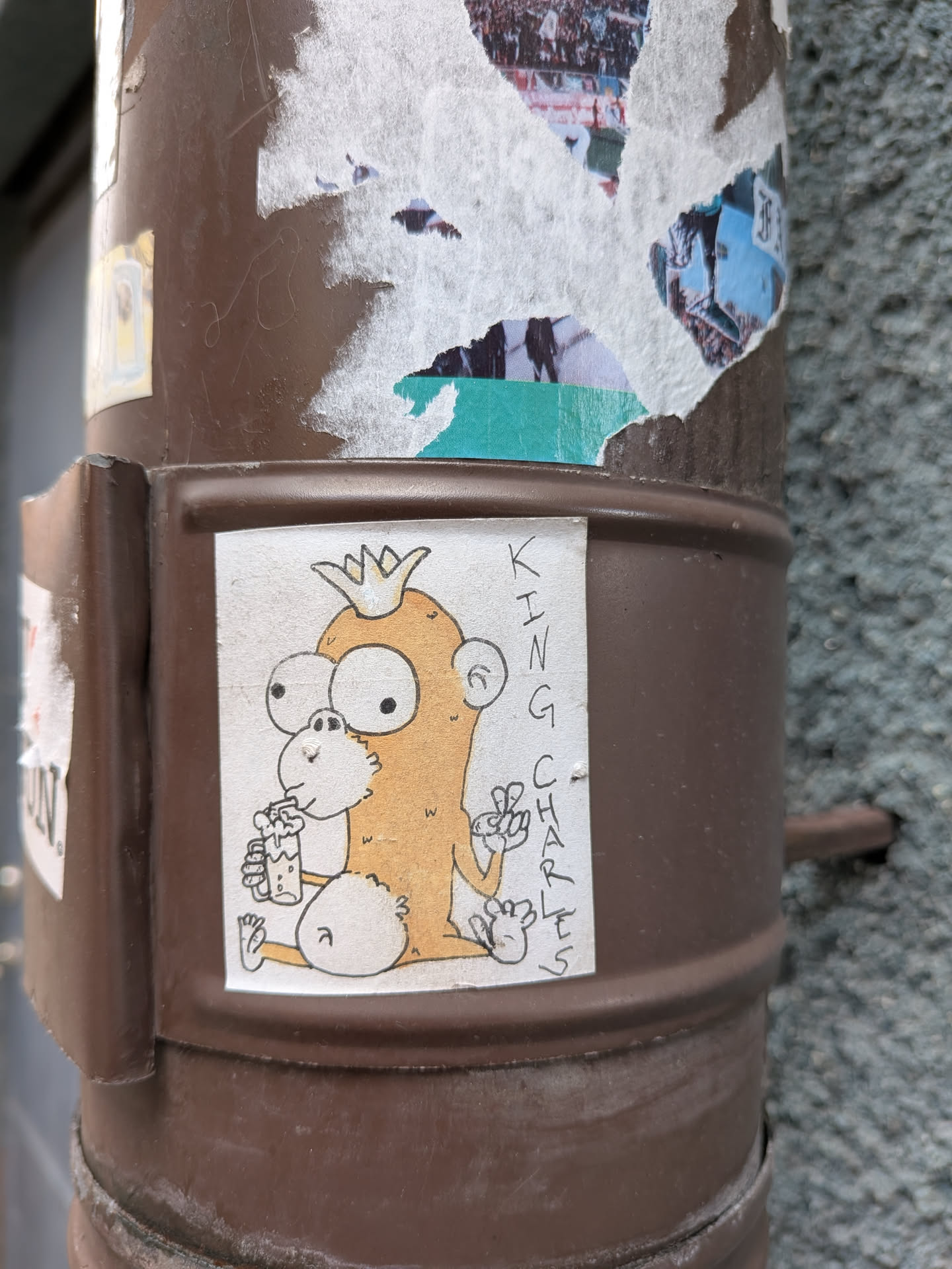 The sticker features a cartoonish, light orange monkey wearing a gold crown. It has large, wide eyes with black pupils and a small, white nose. The monkey is holding a glass filled with a frothy, light-colored beverage in its left hand, and its right hand is raised with two fingers extended in a peace sign. Its body is round and chubby, with fluffy white accents on its lower body and ears. The background of the sticker is white, and the outline and details are in black ink. To the right of the monkey, the words 'KING CHARLES' are written vertically in black, slightly stylized block letters.