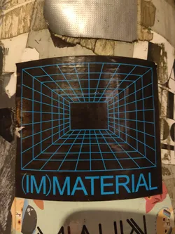 A dark sticker with a cyan grid forming a perspective cube and the text (IM)MATERIAL in cyan. 