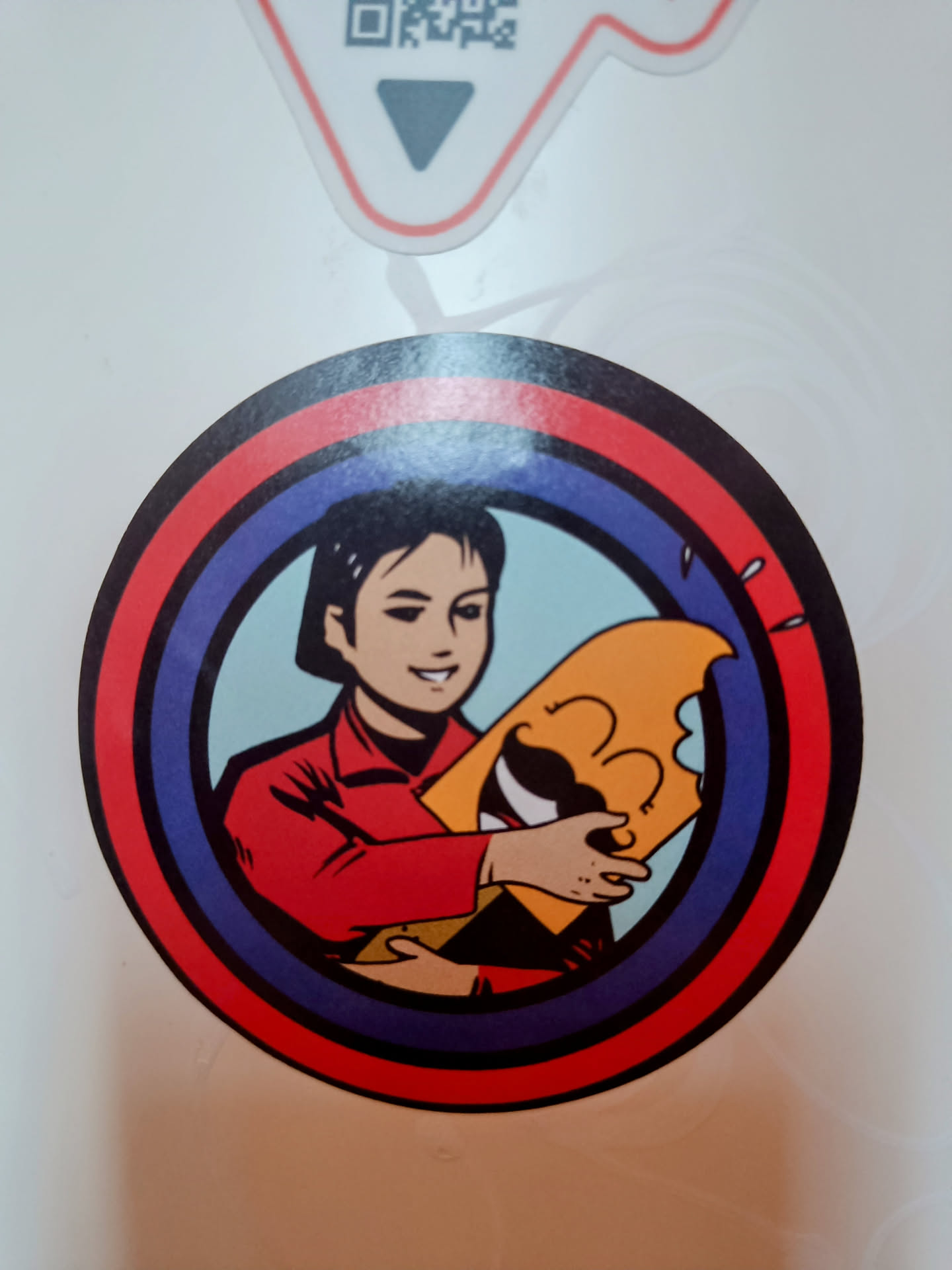 Round sticker featuring a cartoon-style illustration of a person in red clothing holding a large popsicle. The sticker has concentric circles in red, blue and white.
