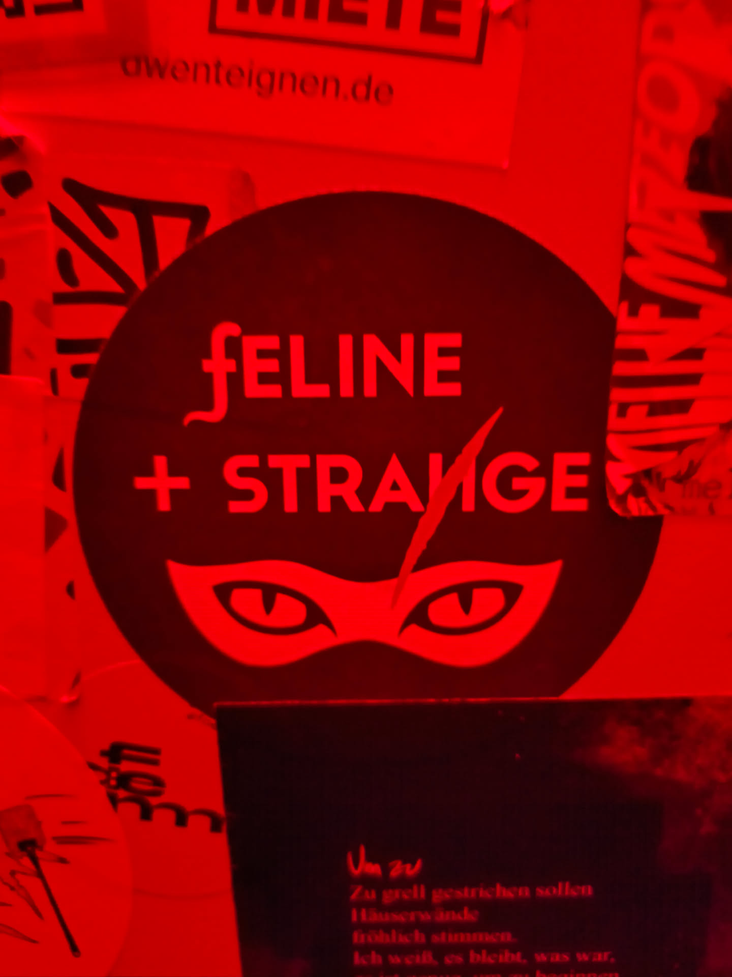 Red round sticker with the text "FELINE + STRANGE" and a cat mask graphic. The sticker has a bold and edgy design.