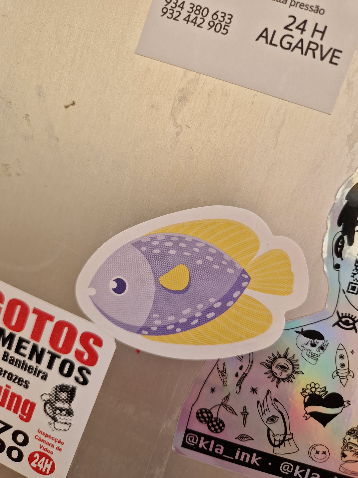 A sticker featuring a cartoon fish with purple body, yellow fins and tail, and white dots. It has a simple, cute design.