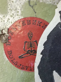 A round sticker featuring a black skeleton meditating in a red circle. The Cyrillic text on the sticker reads  'БОЛЬШЕВИКИ'.  The sticker is weathered and slightly damaged.