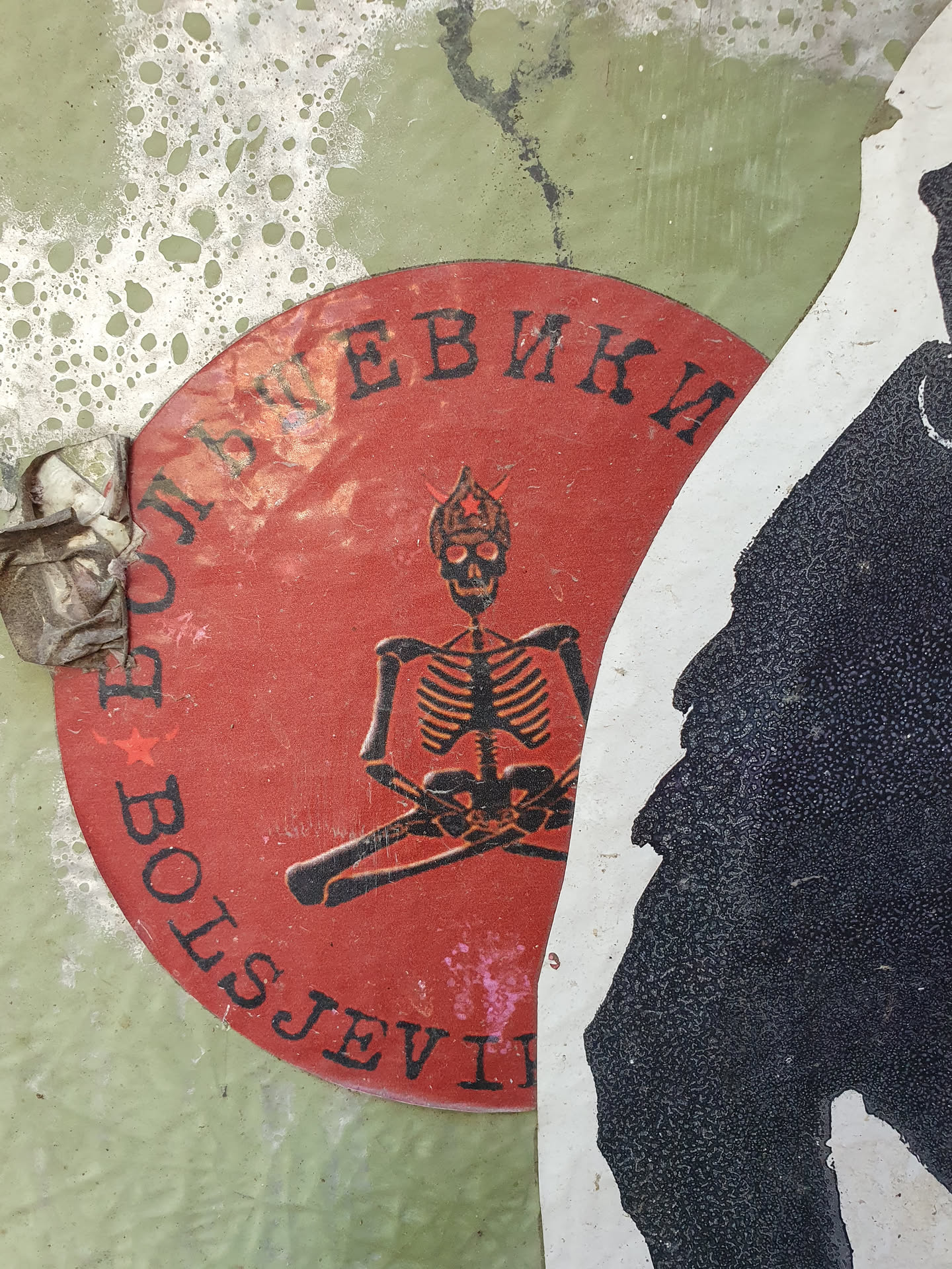 A round sticker featuring a black skeleton meditating in a red circle. The Cyrillic text on the sticker reads  'БОЛЬШЕВИКИ'.  The sticker is weathered and slightly damaged.