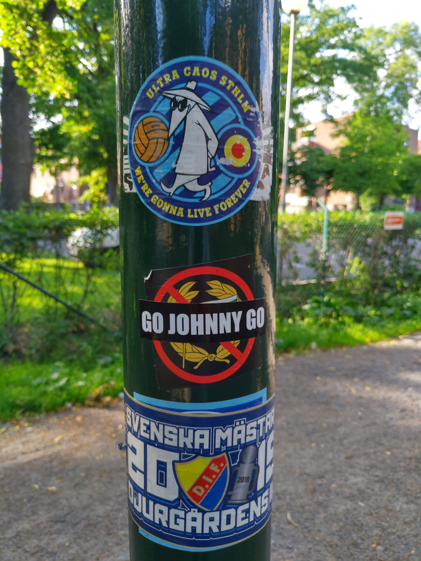 A sticker with the text "GO JOHNNY GO" crossed out with a red circle. The sticker is on a green pole, and there are other stickers around it.