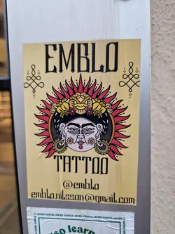 Sticker with a traditional tattoo-style illustration of a face surrounded by a sun and flowers.  The sticker includes the brand name, social media handle, and email address.