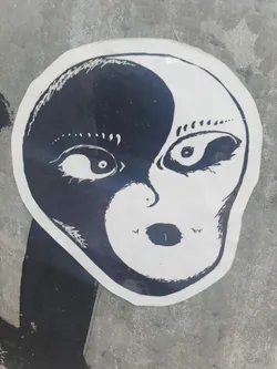 A black and white sticker with an illustration of an alien face split in half, representing the concept of yin and yang. The style is simplistic and slightly eerie.