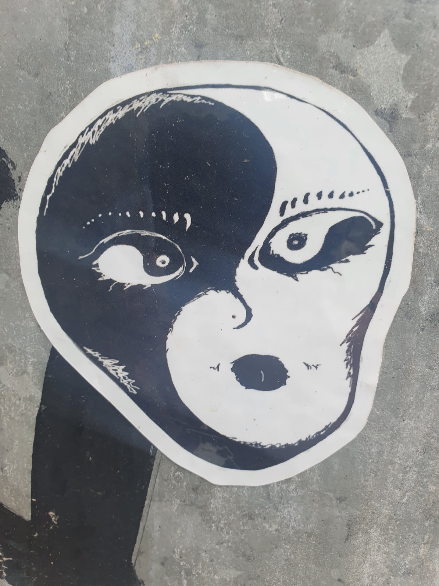 A black and white sticker with an illustration of an alien face split in half, representing the concept of yin and yang. The style is simplistic and slightly eerie.