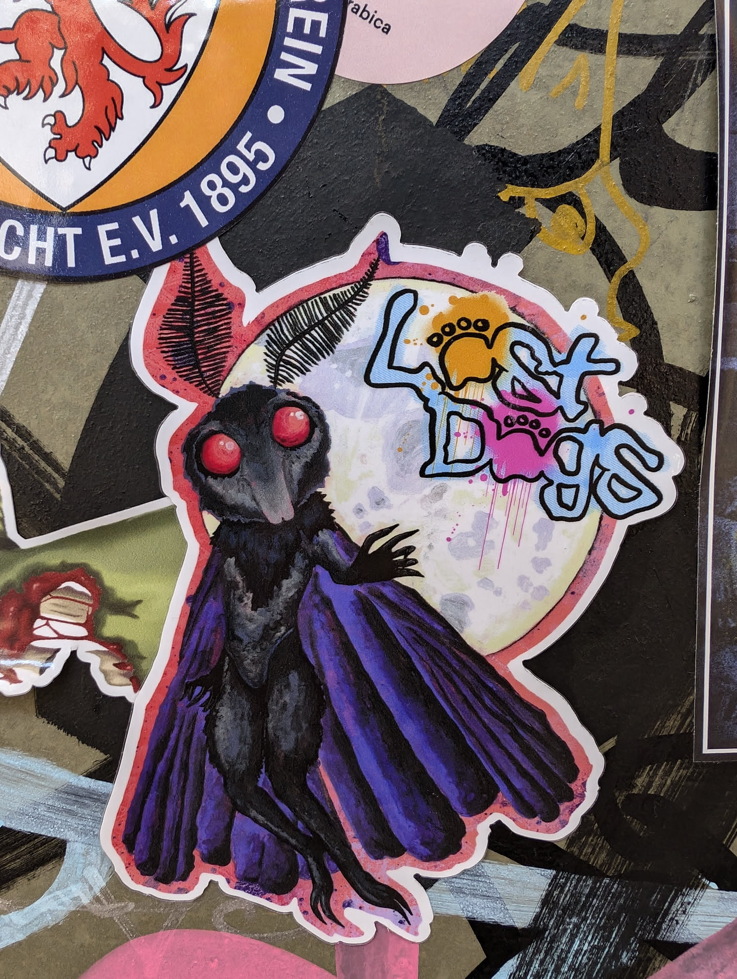 A watercolor sticker featuring a mothman-like creature with large red eyes, set against a moon backdrop. The words "Last Days" are stylized and incorporated into the design.