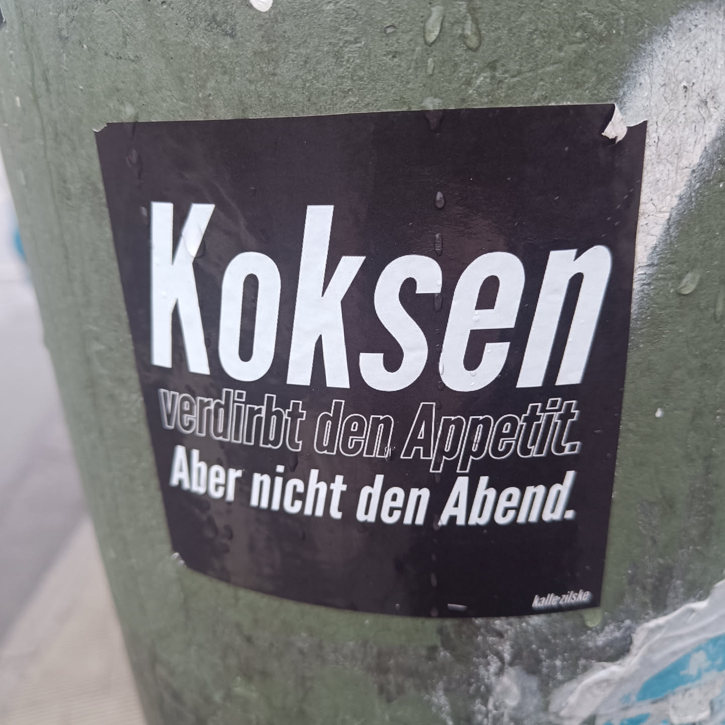 A black sticker with white text on it. The text says: "Kokosen verdirbt den Appetit. Aber nicht den Abend." which translates to: "Cocaine spoils the appetite. But not the evening."