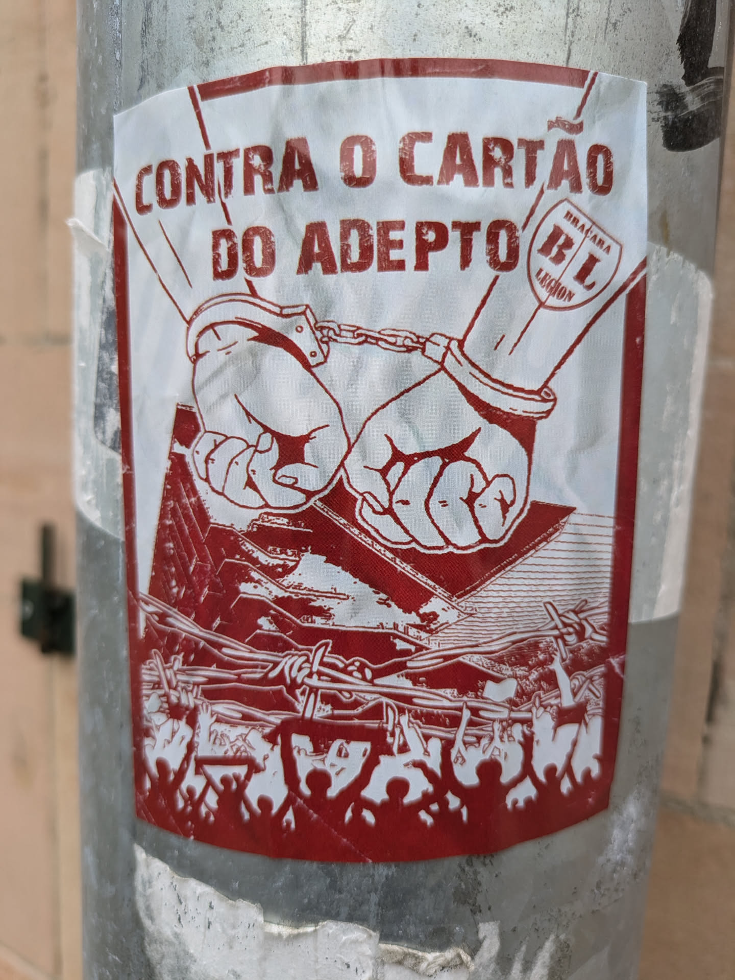 Red and white sticker with an illustration of two handcuffed hands over a barbed wire fence and a crowd of people. The text says "Contra o Cartão do Adepto" which translates to "Against the Fan Card".  There is also a logo that appears to be from Bracara Legion.
