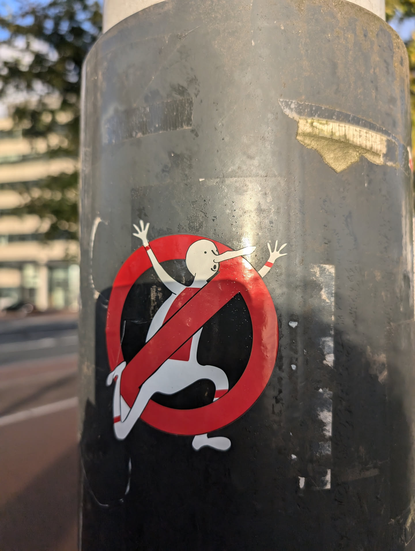 A round sticker with a red prohibition symbol and a cartoonish figure running inside it. The figure has a long nose and is depicted with a simplistic style.
