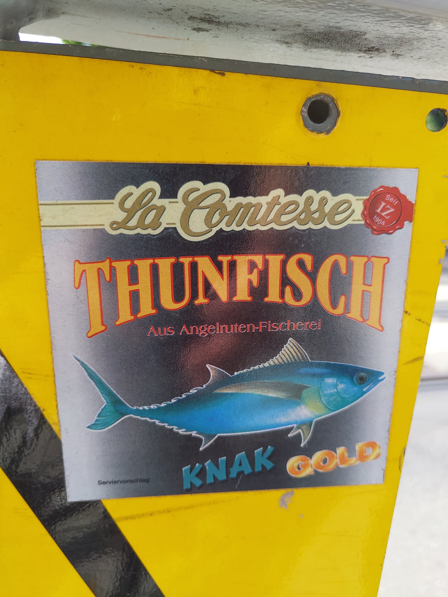 A vintage sticker featuring a tuna fish illustration.  The text includes "La Comtesse Thunfisch" and "Knak Gold", suggesting a brand of tuna. There is also smaller text indicating it's from  "Angelruten-Fischerei" (angling fishery).