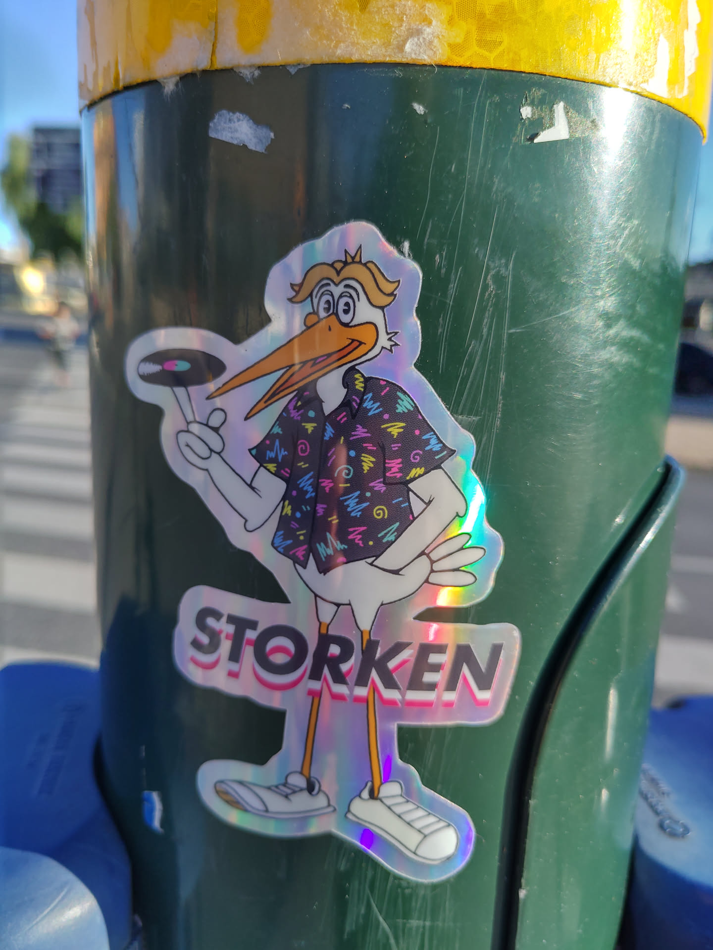 Holographic sticker of a stork wearing a 90s-style shirt and holding a vinyl record. The text 'STORKEN' is written below the stork.