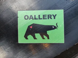 Green sticker with a black bear smoking a cigarette and a heart on its back. The text 'OALLERY' is written at the top of the sticker. 