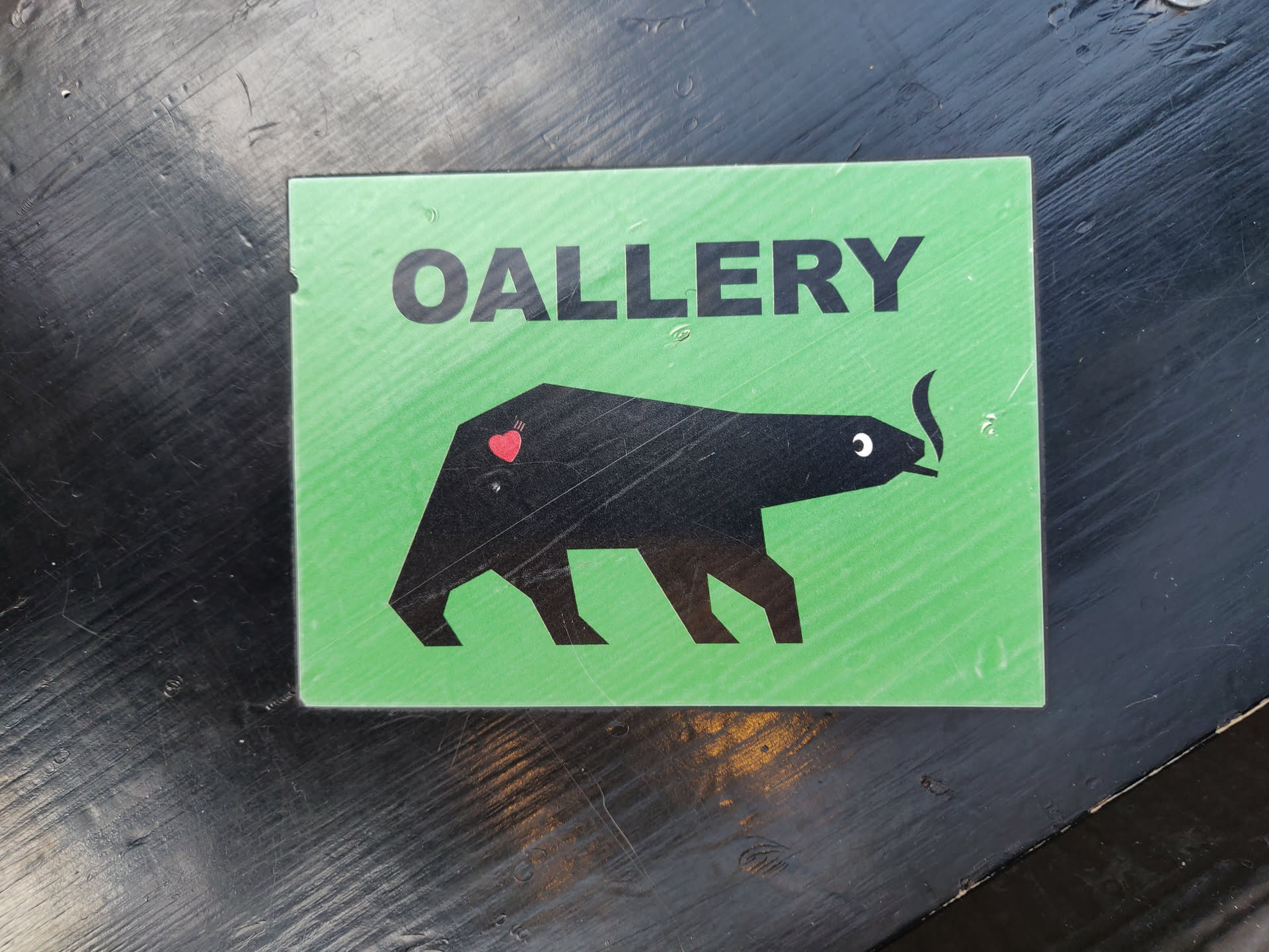 Green sticker with a black bear smoking a cigarette and a heart on its back. The text 'OALLERY' is written at the top of the sticker. 