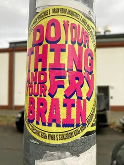 Round yellow sticker with a text message in pink and blue. The text says: Do Your Thing And Fry Your Brain.  There is also a repeating pattern of Brain Frier Industries around the edge of the sticker.