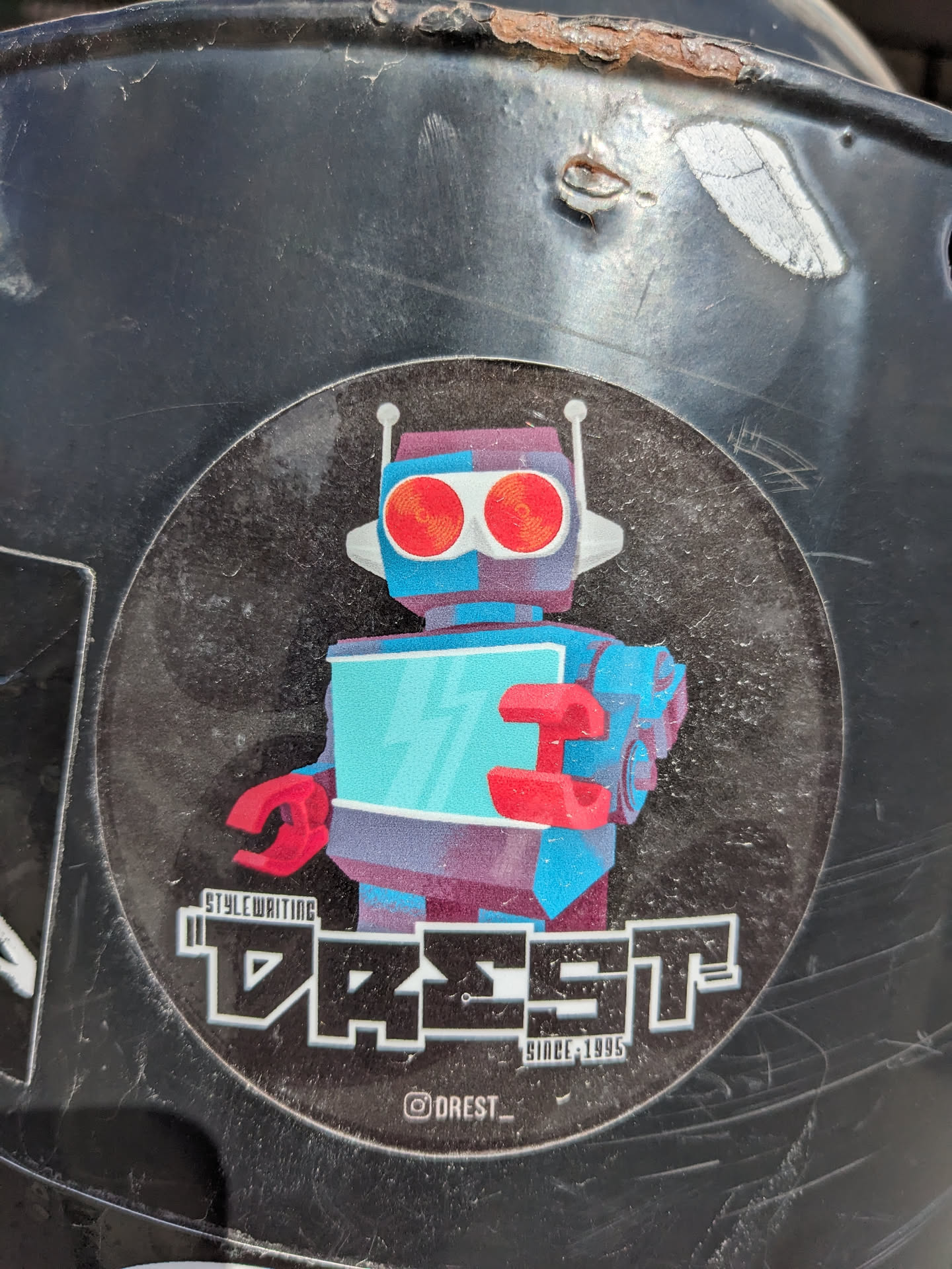 Round sticker featuring a retro-futuristic robot illustration with red eyes and a teal body. The text 'DREST' is prominently displayed below the robot in a stylized font, along with 'STYLEWRITING' and 'SINCE 1995'.  An Instagram handle is included at the bottom.