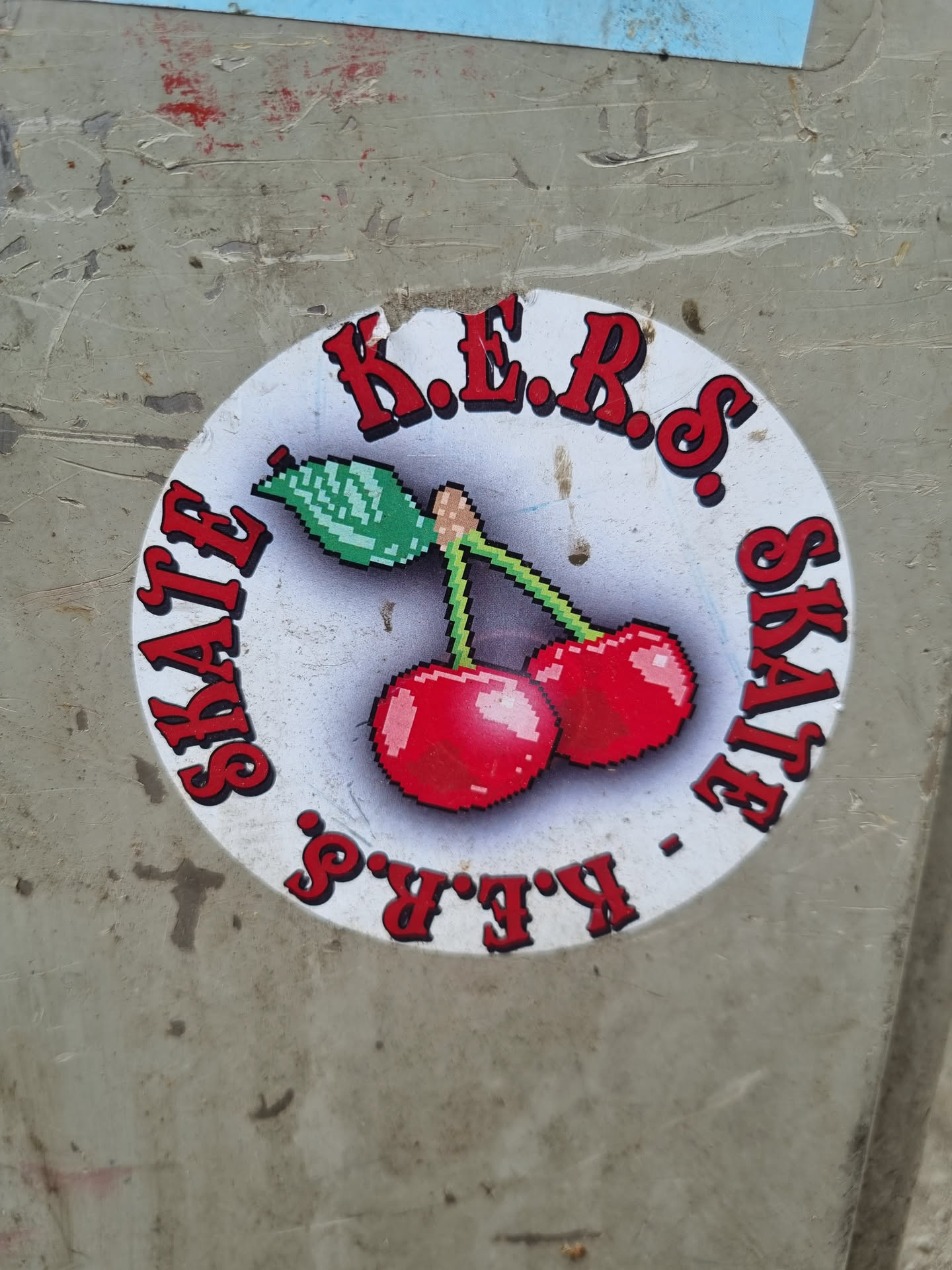 Round sticker with pixel art of two cherries and text in a circle. The text says K.E.R.S. SKATE K.E.R.S..