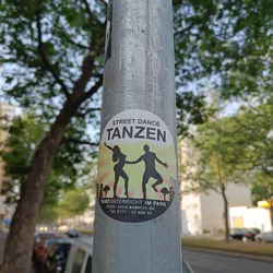 A sticker advertising dance classes in a park.  The sticker features silhouettes of a man and woman dancing against a sunburst background.  Contact information is provided on the sticker.