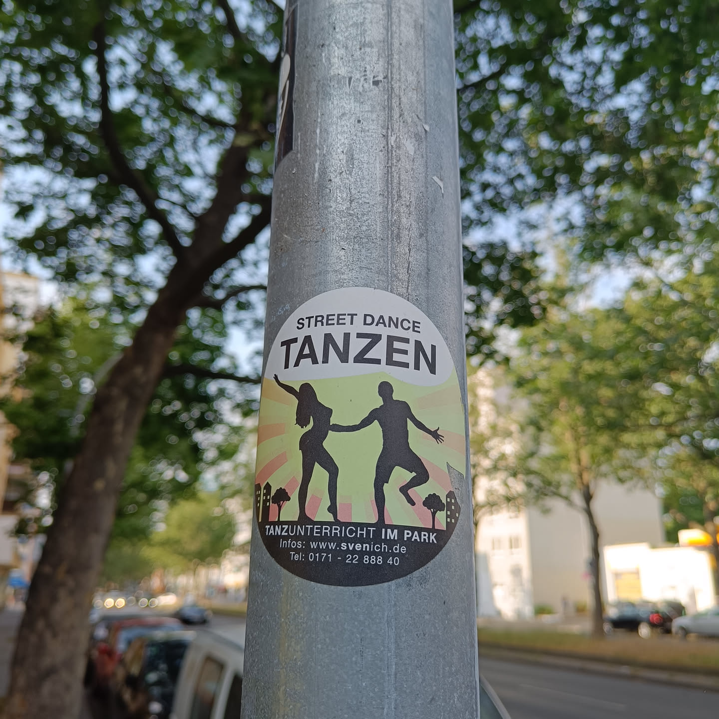 A sticker advertising dance classes in a park.  The sticker features silhouettes of a man and woman dancing against a sunburst background.  Contact information is provided on the sticker.