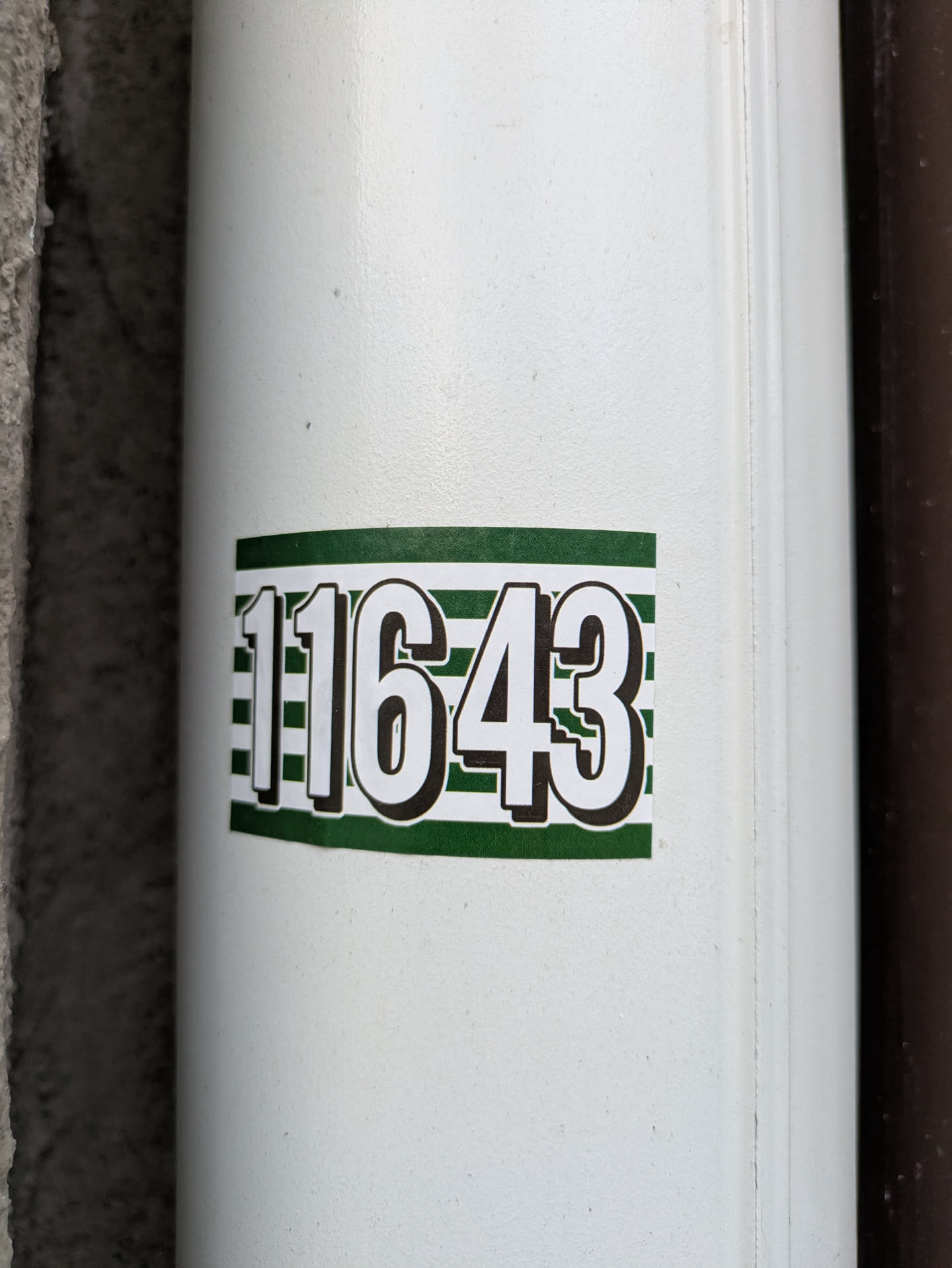 A close-up shot of a white sticker with the number 11643 printed in bold, black text on a green and white striped background.  It's affixed to a white cylindrical surface, possibly a pipe or column.