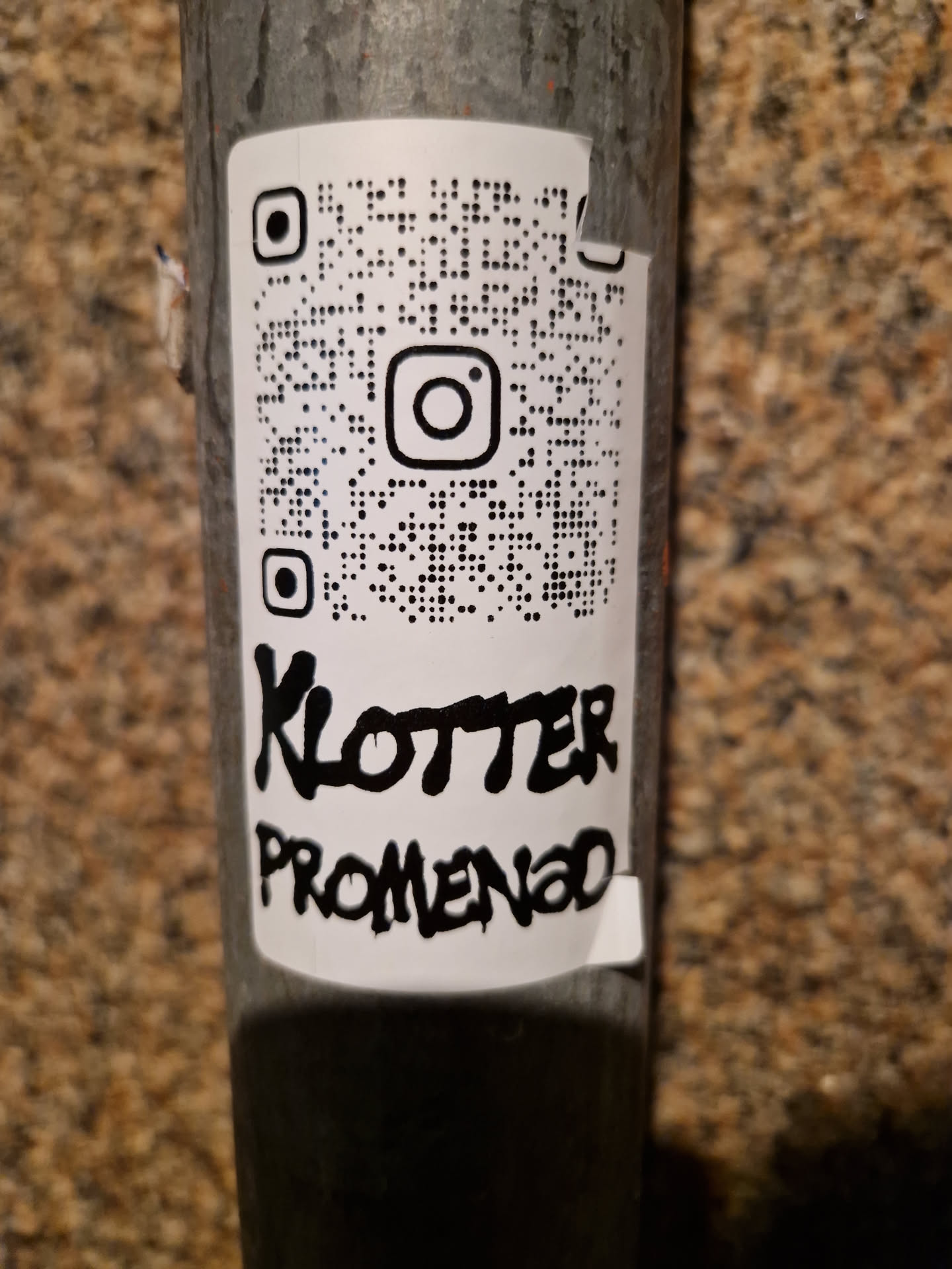 A white sticker with a QR code linking to Instagram and text saying "Klotter Promenad" in black graffiti style.