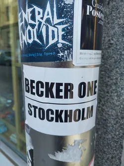 A sticker with the text Becker One Stockholm on a white background. The sticker is attached to a pole. There are other stickers on the pole as well.